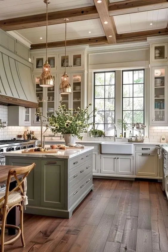 Muted green cabinets create a calming atmosphere. White countertops and bronze pendant lights add a modern touch. Exposed wooden beams and an apron sink complete the farmhouse look. This design works well for compact kitchen remodel ideas.