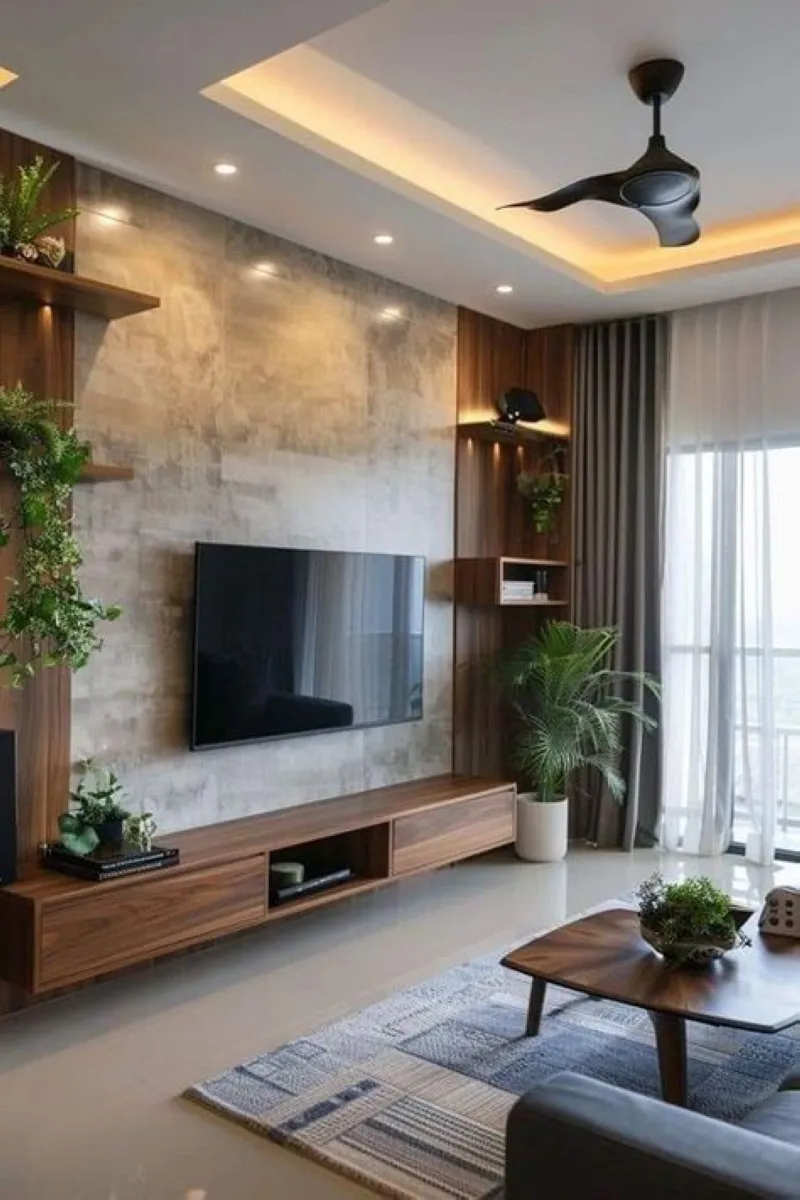 Industrial Charm with Green Accents A TV wall blends concrete texture with wooden floating shelves. Decorative plants and built-in lighting elevate the look, balancing industrial ruggedness with natural elements for a cozy feel.