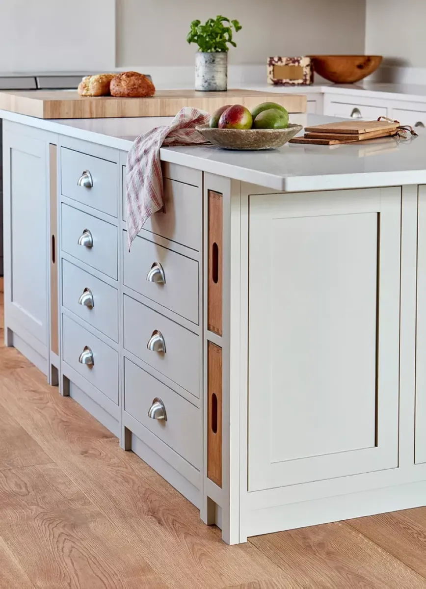 Timeless Simplicity: A Classic White Kitchen Island This island combines sleek white cabinetry with brushed metal handles for a polished, timeless look. The natural wood accents add warmth, making it ideal for a cozy kitchen atmosphere. To achieve this style on a budget, consider repainting existing cabinets and replacing handles with affordable options from secondhand stores or online marketplaces. A simple fruit bowl and fresh herbs bring life to the space without overwhelming the design.