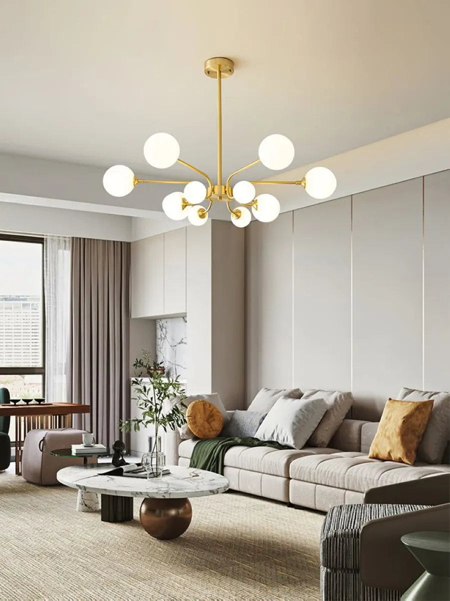 Chandeliers bring a sense of grandeur to living rooms. The featured chandelier here combines gold accents with globe lights, striking the perfect balance between luxury and modernity. This design enhances the neutral backdrop and adds a dynamic focal point above the seating area. 