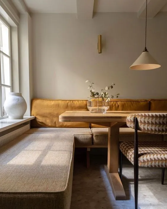 Sleek and neutral-toned corner dining nook with a tufted bench, modern decor, and soft lighting, combining comfort and elegance.