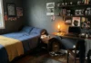 Your Son Wants a Dark Bedroom. Here’s Why He’s Right. Dark bedroom ideas for teenage boys with charcoal walls, warm desk lamp light, and mustard accent throw.