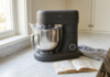 Colored Kitchen Appliances Are Having a Moment. Here’s How to Not Regret Yours Caviar gray stand mixer on a white marble countertop mid-use, with cookie dough and flour, in a bright neutral kitchen