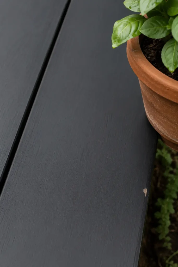 Matte charcoal solid deck stain on pine board, flat even coverage with terracotta pot creating contrast.