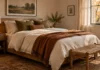 The Fall Bedroom Edit: Three Changes, No Seasonal Clutter Small fall bedroom with ivory bedding, a rust throw, olive cushions and a warm lamp
