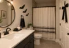 Halloween Bathroom Decor That Keeps the Room Usable Small Halloween bathroom with black paper bats by a mirror, clear sink, washable tray and dark ribbon on the door.