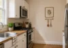 Blank Kitchen Wall Ideas for Small Spaces: Four Zones to Plan Illustrative small apartment kitchen: a blank cabinet-end wall holds a framed botanical print and narrow utensil rail away from the stove, with white cabinets and an oak countertop.