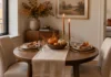 Fall Centerpiece Ideas for a Small Dining Table That Still Fits Dinner Small round dining table with a runner, taper candles, a bowl of mini pumpkins and two place settings in a fall dining nook