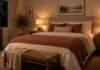 What Color Light Bulb Is Best for a Cozy Bedroom? Cozy bedroom at night lit by two warm white bedside lamps over a bed with cream and rust bedding