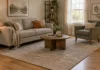 How Big Should a Rug Be in a Small Living Room? Small living room with a sofa and armchair with their front legs on a neutral area rug and bare wood floor around it